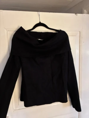 Svart stickad offshoulder tröja Gina Tricot - Stilren svart stickad offshoulder tröja från Gina Tricot med långa ärmar. Tröjan har en enkel, elegant design och är perfekt för att lyfta vilken outfit som helst. Tillverkad i mjukt material som känns skönt mot huden. Passar L/XL