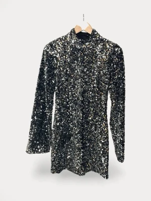 Twist&Tango Glittrig svart paljettklänning - Supersnygg svart kortklänning täckt av glittrande paljetter. Klänningen har lång ärm, hög hals och en öppen rygg som ger en extra wow-effekt. Perfekt för dig som vill sticka ut och glänsa på nästa event.