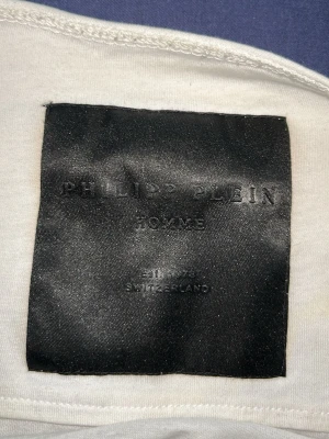 Vit t-shirt med paljetter från Philipp Plein - Säljer en vit t-shirt från Philipp Plein med coola paljettdetaljer på bröstet. T-shirten har korta ärmar och är tillverkad i mjuk bomull. Perfekt för dig som vill sticka ut med en exklusiv look.
