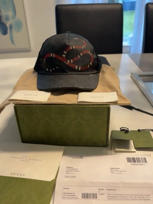 Gucci keps  - Snygg svart keps från Gucci med klassiskt GG-monogram och en röd-vit orm broderad framtill. Kepsen har böjd skärm och mesh på sidorna för extra ventilation. Justerbar baktill för perfekt passform. Materialet är en mix av canvas och mesh äkta kommer med med allting kvitto tack från Gucci om mer frågor är det bara att skriva