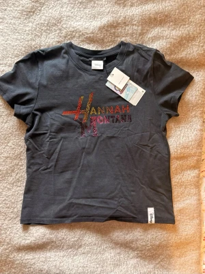 Grå/Svart Hannah Montana t-shirt 🎸 - Cool Grå/Svart t-shirt från Zara med färgglatt Hannah Montana-tryck i strass på bröstet. T-shirten har korta ärmar, rund halsringning. Perfekt för dig som gillar retro och popkultur! 🎸🎉🤗                       Pris går att diskutera! 