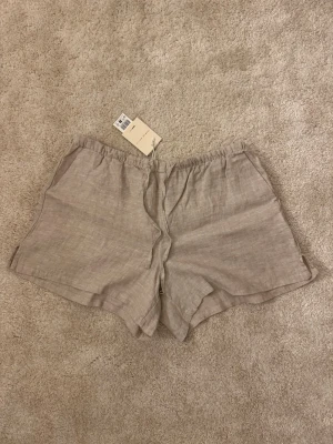 Beige linneshorts med resårmidja - Snygga och luftiga beige shorts i linne med resår i midjan och avslappnad passform. Perfekta för varma dagar och enkla att matcha med olika toppar. Shortsen har en stilren look och är superbekväma.