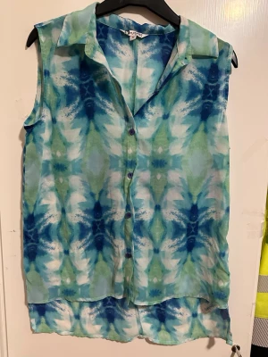 Mönstrad ärmlös blus från Instinct - Säljer en ärmlös blus från Instinct i storlek 36. Blusen har ett coolt blågrönt mönster, knappar framtill och klassisk krage. Materialet är tunt och luftigt, perfekt för varma dagar. Passar dig som gillar färg och att sticka ut!