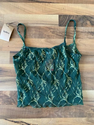 Grön spetsig linnetopp från Flirt Lingerie - Snygg grön linnetopp från Flirt Lingerie med transparent spets och tunna axelband. Mönstret är elegant och toppens material känns lätt och luftigt. Perfekt för att skapa en trendig look. Väldigt fairycore och whimsygoth💕