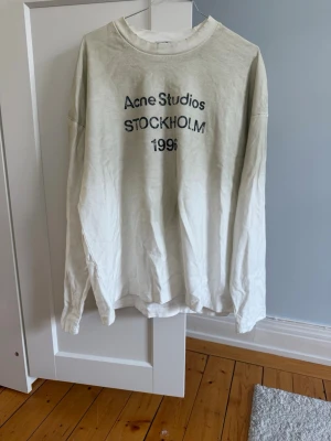 Vit sweatshirt Acne Studios - Vit långärmad sweatshirt från Acne Studios med tryck i svart text på bröstet där det står 'Acne Studios STOCKHOLM 1996'. Tröjan har rund halsringning och avslappnad passform. Perfekt för en clean och stilren look.