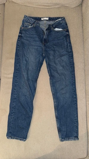 Blå mom jeans med hög midja - Snygga blå mom jeans med hög midja och raka ben. Klassisk femficksmodell med dragkedja och knapp framtill. Jeansen har en vintagekänsla och är tillverkade i 100% bomull. Perfekta för en avslappnad och trendig look.