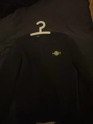 Svart tröja från Stone Island - Snygg svart tröja från Stone Island med den klassiska loggan broderad på bröstet. Tröjan har rund halsringning och lång ärm, perfekt för en stilren och enkel look.