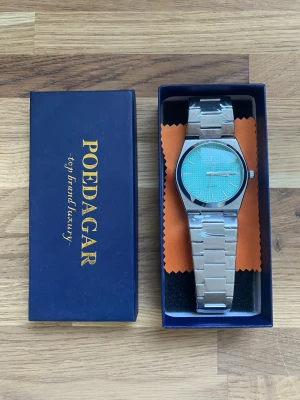 Poedagar herrklocka kvartz 41mm med turkos urtavla - Stilren klocka från POEDAGAR med silverfärgad länk i metall och en blå urtavla med diskret rutmönster. Klockan har minimalistisk design med tydliga visare och index, perfekt för dig som gillar en modern look.