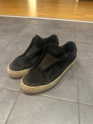 Axel Arigato slip-on sneakers – svarta - Säljer ett par stilrena slip-on sneakers från Axel Arigato i svart mocka. Minimalistisk design som passar både vardag och mer uppklädda outfits. Bekväma och lätta att ta på🤍 Skorna är använda som man kan se, de har normalt slitage, främst synligt på sulorna och lätt på mockan (se bilder). Inget som påverkar funktionen.  Det är bara komma med frågor eller om ni vill se fler bilder🥰
