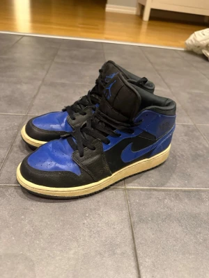 Air Jordan 1 Mid svart/blå - Säljer ett par snygga Nike Air Jordan 1 Mid i svart och blå färgkombination 🖤💙 En klassisk modell som passar perfekt till både streetwear och vardagslook. Skorna är använda och har normalt slitage, se bilder för detaljer. Lite veck framtill och något gulnad sula förekommer, men de är fortfarande i fint skick och har mycket kvar att ge. Ett stilrent och tidlöst par sneakers som lyfter vilken outfit som helst.                                                                   Skriv vid funderingar🤍