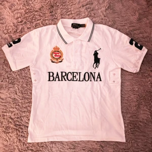 Vit Chief Keef Polo Barcelona piké - Vit piké från Polo Ralph Lauren med klassisk pikékrage, svart broderad logga och stor text 'Barcelona' framtill. Stilren och prydlig. Hör av dig vid intresse👋
