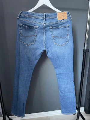 Blå jeans från Jack & Jones - Snygga blå jeans från Jack & Jones med klassisk femficksdesign och raka ben. Jeansen har ljus tvätt och subtila slitningar framtill för en avslappnad look. Perfekta för dig som gillar en enkel och stilren stil.