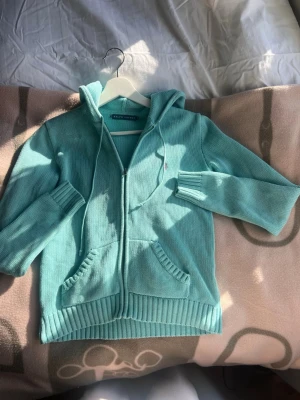 Turkos stickad hoodie från Ralph Lauren - Turkos stickad hoodie från Ralph Lauren med dragkedja framtill, två fickor och ribbade muddar. Klassisk huva med dragsko och liten rosa broderad logga på bröstet. Perfekt för en chill och avslappnad stil.