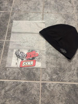 SYNA world - Svart mössa från SYNA med broderad logga framtill. Enkel och stilren design, perfekt för att hålla värmen och ge en urban touch till din outfit. Mössan är mjuk och stretchig, passar de flesta huvudstorlekar. Medföljer tags o bags