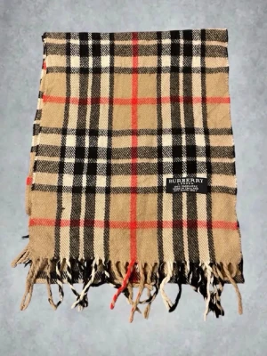 Burberry halsduk  - Snygg halsduk från Burberry i beige med klassiskt rutmönster i svart, vitt och rött.  Perfekt accessoar för att lyfta din outfit.                   Skick 9/10
