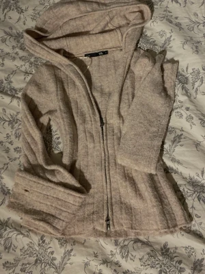 Beige stickad hoodie med dragkedja - Mysig beige stickad hoodie från Gina Tricot med hel dragkedja framtill och huva. Tröjan har en lätt ribbad struktur och är perfekt för en avslappnad stil. Passar dig som gillar en enkel och stilren look.