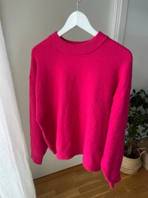 Rosa stickad tröja från H&M - Säljer en ceriserosa stickad tröja från H&M med rund halsringning och ribbade muddar. Tröjan har en avslappnad passform och är perfekt för att addera färg till din outfit. Materialet är mjukt och skönt, perfekt för kyligare dagar.