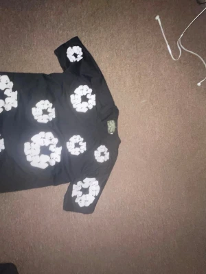 Svart t-shirt denim tears  - Svart t-shirt från Denim & Marcs med stora vita blommönster över hela framsidan. Klassisk rund hals och korta ärmar. Perfekt för dig som vill sticka ut med en unik och cool design. Tillverkad i mjuk bomull för skön känsla.