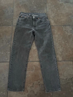 Grå raka jeans från Levi's - Ett par grå jeans från Levi's med rak passform och klassisk femficksdesign. Jeansen har hög midja, knappgylf och är tillverkade i slitstark denim. Perfekta för en avslappnad och trendig look.