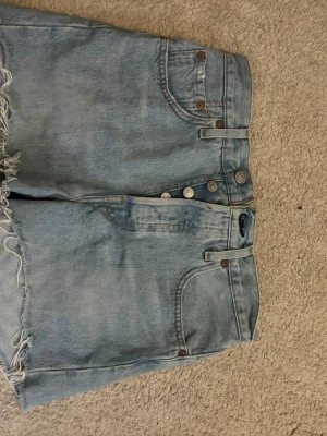 Levi's ljusblå jeansshorts med rå kant - Ljusblå jeansshorts från Levi's med hög midja, klassiska fem fickor och rå, fransig kant nedtill. Shortsens material är slitstark denim och de har knappgylf framtill. Perfekta för en avslappnad och trendig look.