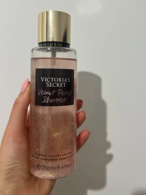 Victoria's Secret Velvet Petals Shimmer - En lyxig shimmer body mist från Victoria's Secret i doften Velvet Petals Shimmer. Flaskan är genomskinlig med rosa skimmer och har en elegant guldfärgad kork. Innehåller 250 ml och ger både doft och glittrande effekt på huden. Använd ett fåtal gånger.