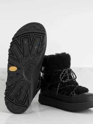 Svarta moon boots från UGG - Säljer ett par svarta moon boots från UGG med fluffig ovandel i fårskinn och detaljer i läder. Skorna har grov sula med Vibram-mönster och snörning med reflexdetaljer. Perfekta för kalla dagar när du vill hålla stilen och värmen.