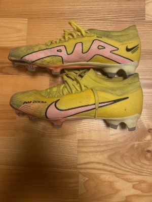 Nike Air Zoom gula fotbollsskor - Säljer ett par gula Nike Air Zoom fotbollsskor med rosa och svarta detaljer. Skorna har snörning, låg profil och är tillverkade i ett lätt syntetmaterial för bästa känsla på planen. Swoosh-logga på sidan och texten 'Air Zoom' tryckt på ovansidan.