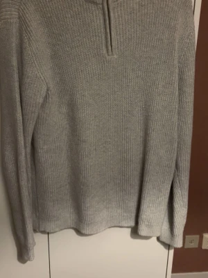 Ljusgrå stickad tröja med dragkedja - En stilren ljusgrå stickad tröja med lång ärm och liten dragkedja vid halsen. Inga skador noppor eller fläckar. 