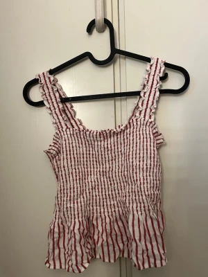 Randig linnetopp från Hollister - Söt randig linnetopp från Hollister i vitt och rött. Toppen har breda axelband med volangkant och stretchig överdel. 