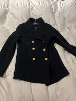 skepparkavaj - Stilren marinblå skepparkavaj från Busnel med dubbelknäppning och sex guldiga knappar framtill. Klassisk krage och två fickor på sidorna. Kavajen har en figurnära passform och dekorativa knappar även baktill. Perfekt för en trendig och tidlös look.