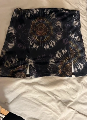 Mini sammet kjol med tie-dye mönster - Säljer en svart kortkjol med tie-dye inspirerat mönster i blått, grått, brunt och vitt. Kjolen har en rak passform och två slitsar framtill. Urban outfiters 
