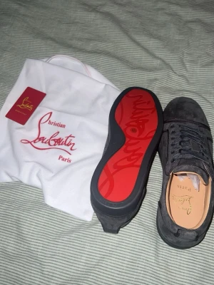 Christian Louboutin , Loubs - Snygga svarta sneakers från Christian Louboutin i mocka med den ikoniska röda sulan. Skorna har låga snörning, diskret logga på innersulan och klassisk siluett. Perfekta för dig som vill ha något exklusivt och stilrent.