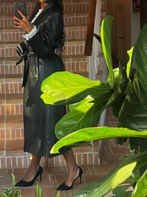 Svart lång skinnjacka - Super fin svart lång skinnjacka från Zara med band i midjan och knappar.  Använd 2 gånger, i mycket fint skick utan märken. Storlek M men passar även S. Köpt för ca 800 kr. 