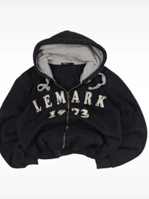 Svart hoodie från Le Mark med dragkedja - Svart hoodie från Le Mark med grått innerfoder i huvan och vita snören. Stor text 'LEMARK 1973' på bröstet i vitt. Dragkedja framtill och ribbade muddar vid ärmar och midja. Perfekt för en avslappnad streetwear-look. Väldigt skön och niche så rekommenderar verkligen!🔥 Priset är såklart diskuterbart🤙