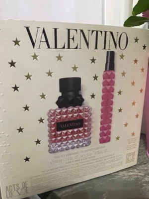 Valentino parfymset med stjärndetaljer - Lyxigt parfymset från Valentino med en rosa, noppad glasflaska och matchande rosa resestorlek. Förpackningen är dekorerad med guldstjärnor och en stor lila rosett, vilket ger en exklusiv känsla. Perfekt present till någon som älskar eleganta dofter.