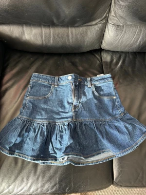 Volangkjol i denim - Snygg jeanskjol från bikbok med volang nertill och klassiska femficksdetaljer. Kjolen är i blå denim och har normal passform med knapp och dragkedja framtill. 