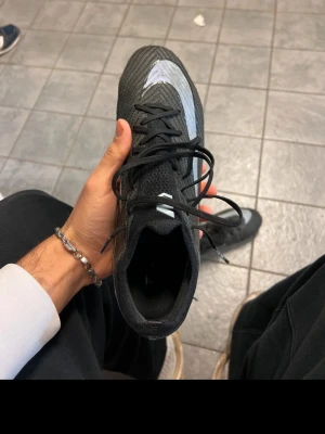 Nike Air Zoom Mercurial Vapor 16 FG - Nike Air Zoom Mercurial Vapor 16 Elite FG Shadow är en fotbollssko i svart med blå detaljer och en stor Nike-logga på sidan. Skon har en låg profil, snörning och FG-dobbar för spel på naturgräs. Ovandelen är tillverkad i syntetmaterial för lätt vikt och bra bollkontroll. Köpta för originalpris 3249 men använda ett antal gånger och säljs därför billigare. Fortfarande jättefräscha dubbar och skick! Vid intresse kan jag skicka bilder!