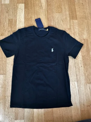 Svart t-shirt från Polo Ralph Lauren - Klassisk svart t-shirt från Polo Ralph Lauren med rund halsringning och den ikoniska broderade loggan på bröstet. T-shirten är kortärmad och tillverkad i mjuk bomull, perfekt för en stilren och enkel look. Hör av er om ni har fler frågor eller vill ha fler bilder! T shorten har endast blivit testad men kvitto finns tyvärr inte 
