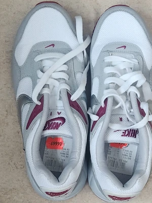 Nike vita och grå sneakers stl.39  - Nike sneakers i vitt och ljusgrått med detaljer i vinrött. Klassisk låg modell med mesh och syntetmaterial, snörning framtill och tydlig Nike-logga på plös och häl. Snygg retrostil som passar till många outfits.