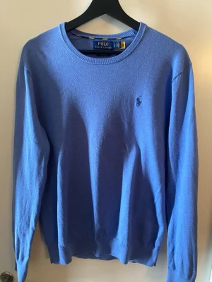 Blå stickad tröja Polo Ralph Lauren - Snygg blå stickad tröja från Polo Ralph Lauren i slim fit-modell. Tillverkad av mjuk Pima bomull och har den klassiska broderade loggan på bröstet..