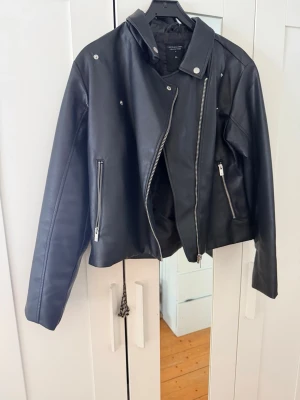 Svart bikerjacka i faux leather 🖤storlek XL - Stilren svart bikerjacka i faux leather med snygga silverdetaljer ✨ Klassisk modell med asymmetrisk dragkedja och fickor framtill. Perfekt både till vardag och kväll – passar till allt från jeans till klänning. Storlek: XL Skick: Fint skick Material: Faux leather Säljes då den inte används längre 🤍