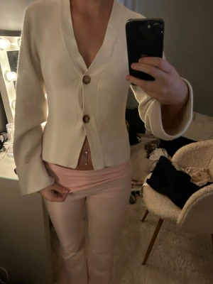 Vit kofta med träknappar - Stilren vit kofta med v-ringning och två stora träknappar framtill. Koftan har långa, lätt utsvängda ärmar och en figurnära passform. Perfekt att matcha med ljusa byxor för en fräsch look. Från ginatricot 