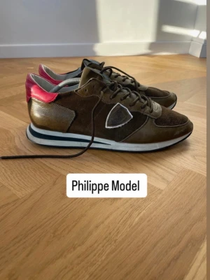 Bruna Philippe Model sneakers - Snygga sneakers från Philippe Model STORLEK 46 i brunt mocka och läder med grå detaljer och en cool rosa häl. Klassisk låg modell med vita och svarta ränder på sulan och logga på sidan. Perfekta för dig som vill ha något unikt och trendigt.