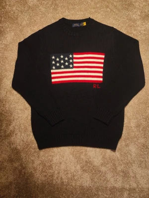 Ralph Lauren - American express - Navy blå - Säljer en riktigt fet och stilig Ralph Lauren American Express tröja med färg Navy blå! Tröjan ger en classy look med den fina blåa färgen och den stora amerikanska flaggan stickad framtill! Hör gärna av dig vid frågor! Den passar de flesta från 1,60-1,75 (Medium