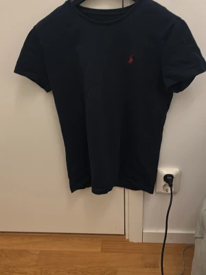t-shirt från Ralph Lauren (lappen är borta) - Klassisk svart t-shirt från Ralph Lauren med röd broderad logga på bröstet. T-shirten har rund halsringning och korta ärmar. Perfekt basplagg med stilren design.