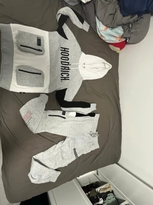 Gråa mjukisbyxor från Hoodrich - Säljer ett par gråa mjukisbyxor från Hoodrich med svarta detaljer och logga på benet. Byxorna har resår i midjan med dragsko och muddar vid bensluten. Perfekta för chill dagar och streetwear-stil.