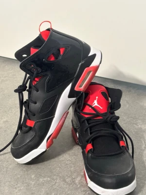 Svarta och röda Air Jordan sneakers - Säljer ett par snygga Air Jordan sneakers i svart och rött med vita detaljer. Skorna har högt skaft, klassisk Jumpman-logga på plösen och cool design med mesh och syntetmaterial. Perfekta för dig som gillar streetwear och basketstil. Knappt använda 