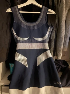 Mini dress - Snygg marinblå kortklänning från Adidas Stella McCartney med vita och gråa detaljer samt grafiskt randigt mönster. Klänningen är ärmlös och har en sportig, modern look med rund halsringning och markerad midja.