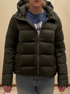 Mörkgrön dunjacka från Colmar - Snygg mörkgrön dunjacka från Colmar med huva och dragkedja framtill. Jackan har en puffig design, två sidofickor och Colmar-logga på ärmen. Perfekt för kalla vinterdagar och riktigt skön att bära tack vare det mjuka dunet.