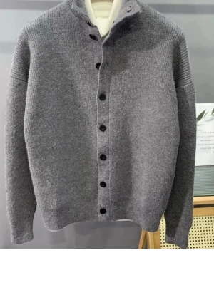 Grå stickad kofta med knappar - Mysig grå stickad kofta med hög krage och svarta knappar hela vägen framtill. Koftan har en rak passform och långa ärmar, perfekt för lager på lager. Enkel och stilren design som passar till det mesta.